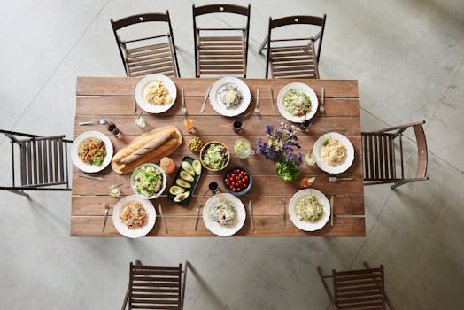 Top view of a wooden table set with pasta dishes, fresh ingredients, and drinks for a cozy meal.
